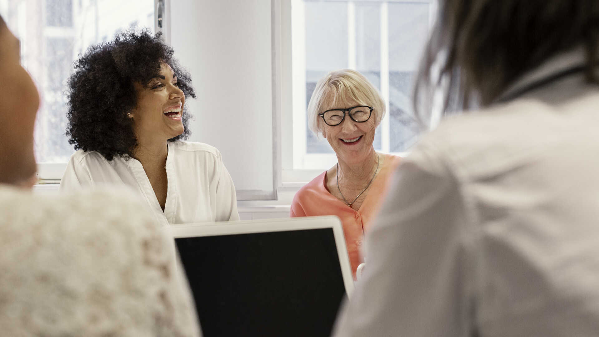 Grupp med människor som skrattar och sitter runt ett bord i ett ljust kontorsrum