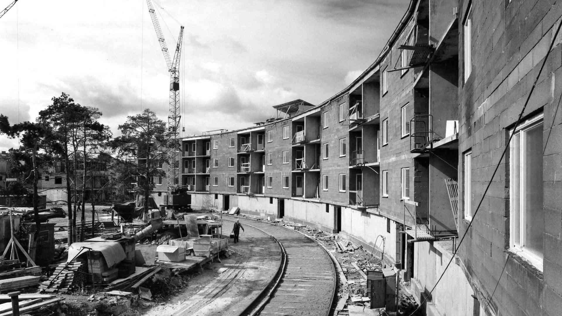 Byggarbetsplats för en bostadsbyggnad i en kurvig form med flera våningar, kran i bakgrunden och byggmaterial runtom