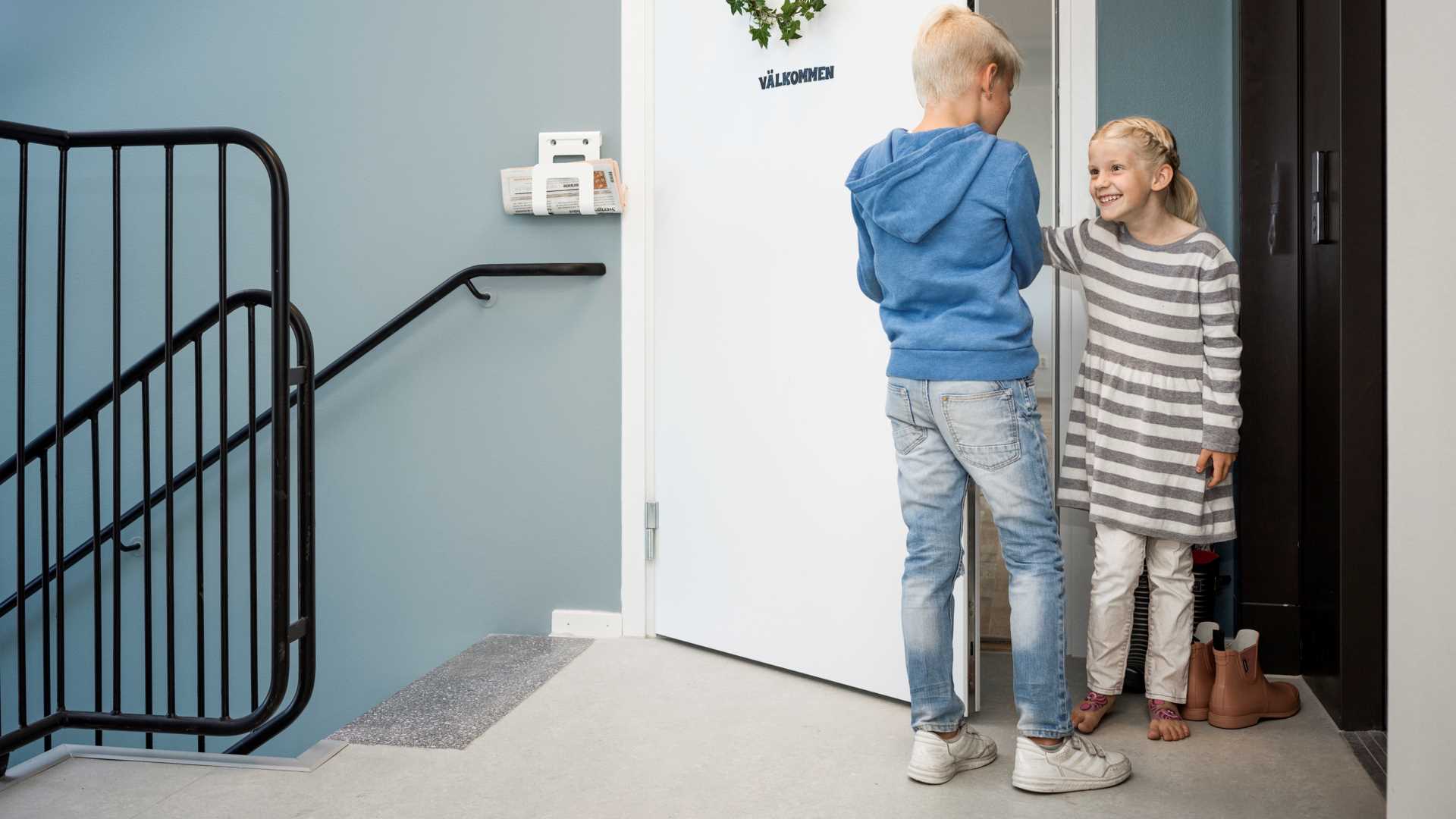 Två barn, en pojke och en flicka, står vid en dörr som är märkt med 