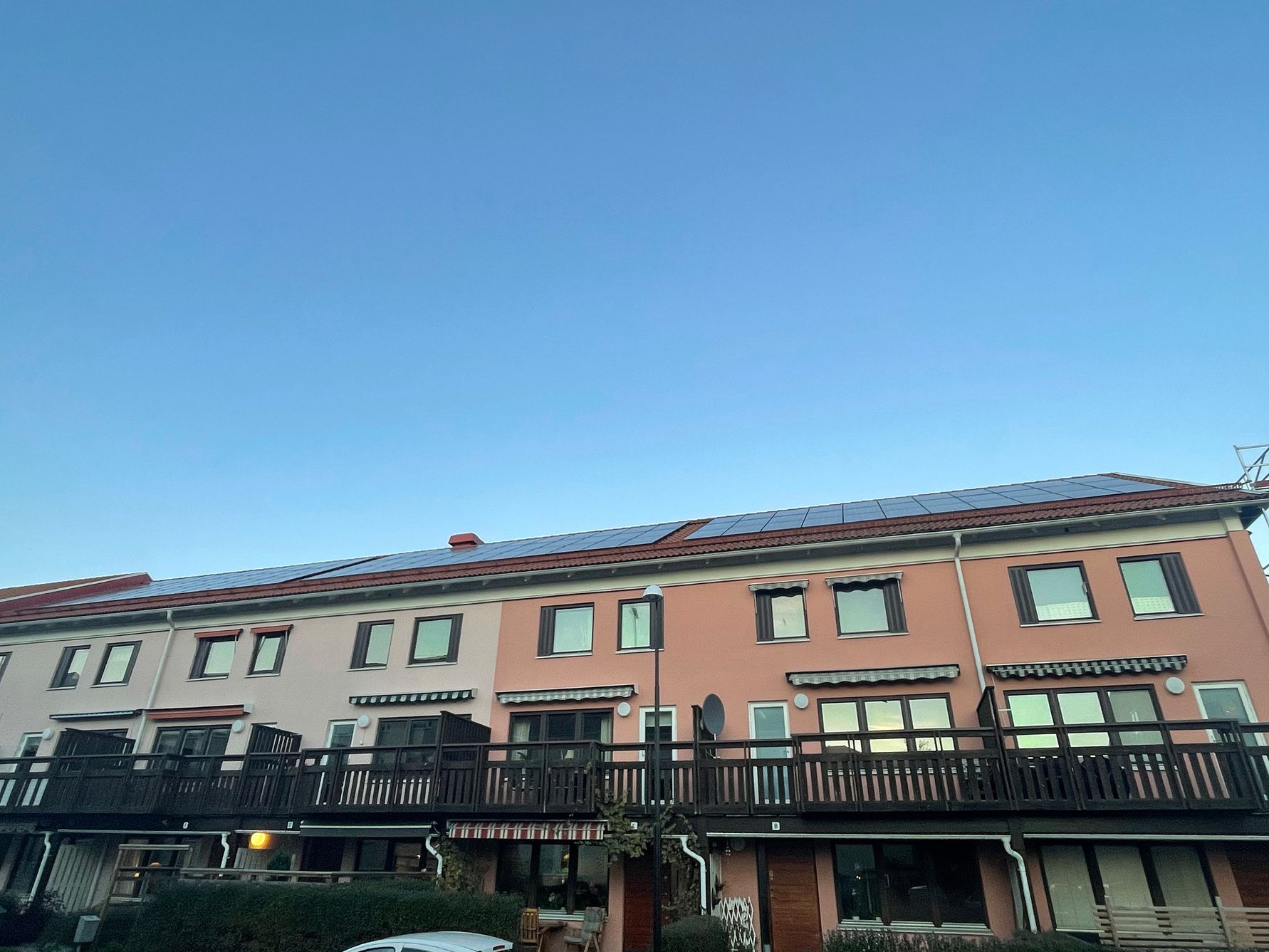 Rad av flerbostadshus med solpaneler på taket under en klar blå himmel