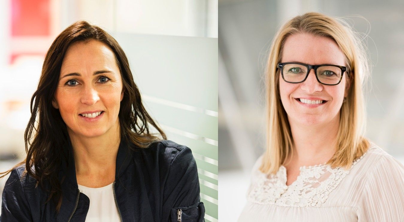 Två kvinnor, en med mörkt hår och vit topp under en mörk jacka till vänster, och en med ljust hår och vit spetsprydd topp till höger, står i en ljus inomhusmiljö