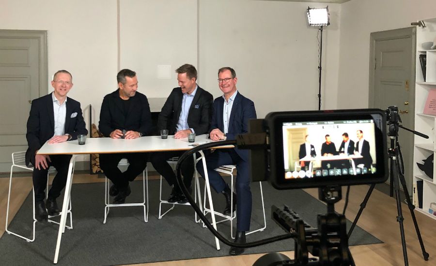 Fyra personer sitter vid ett bord i ett ljust rum, framför en kamera på ett stativ