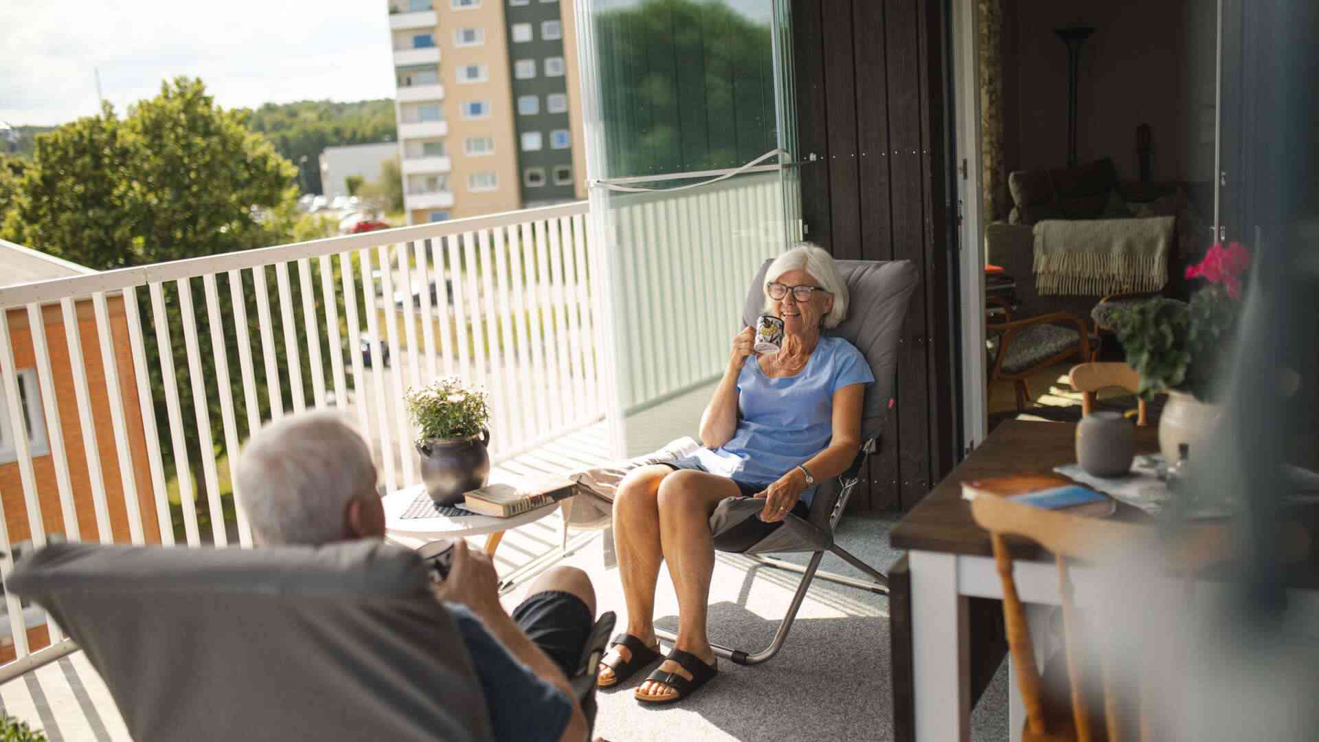 Äldre par som sitter på en balkong, dricker kaffe och njuter av solen