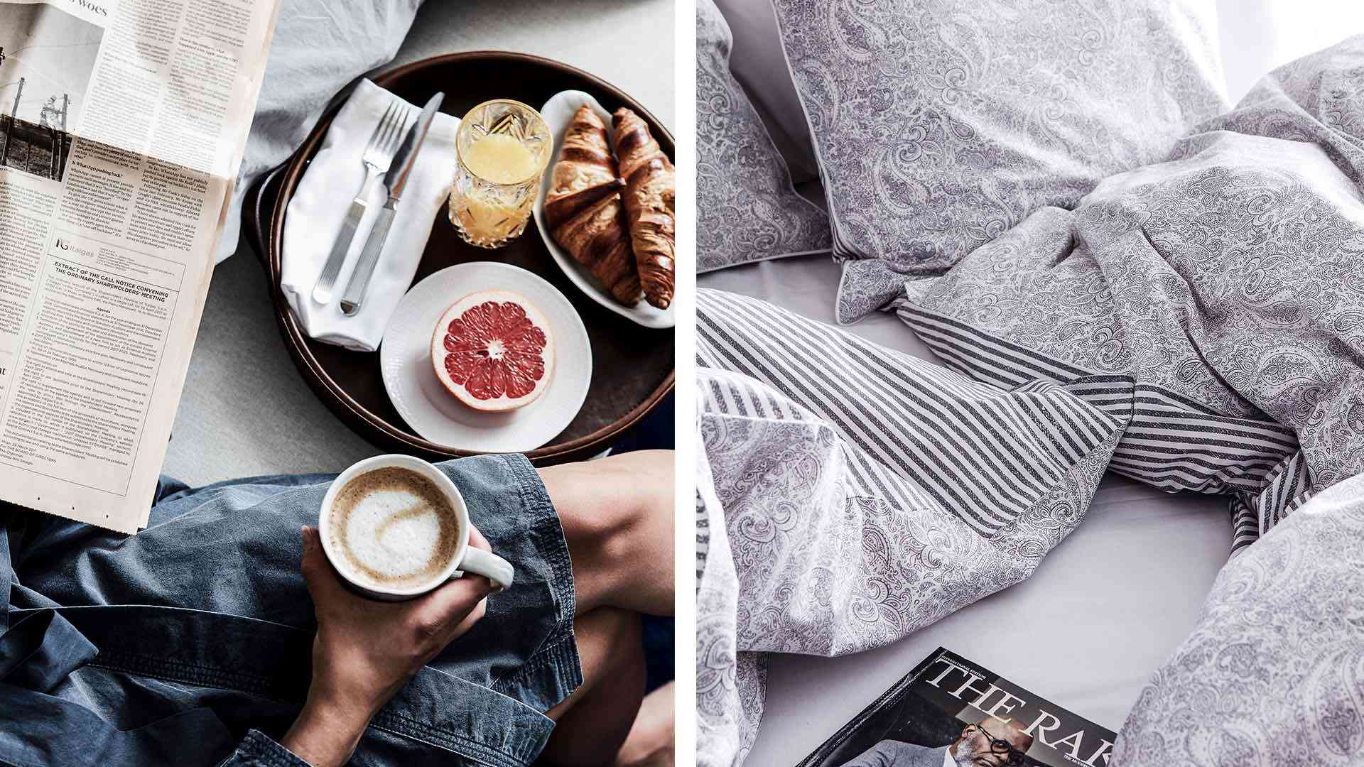 Tidningsläsning på säng med frukostbricka innehållande kaffe, grapefrukt, croissanter och apelsinjuice, samt sängkläder i mönstrat tyg