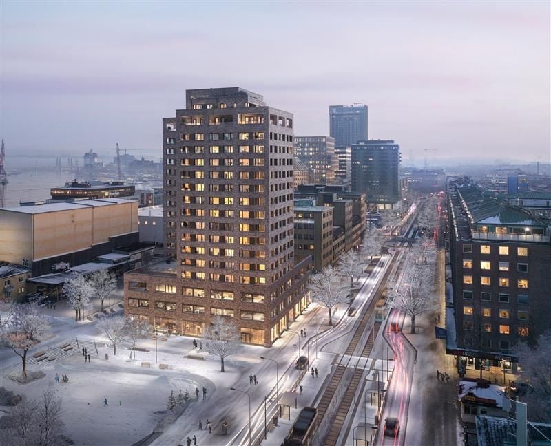 Vy över ett stadskvarter med en höghusbyggnad, snöbelagda gator, träd och spårvagnar på en vinterkväll