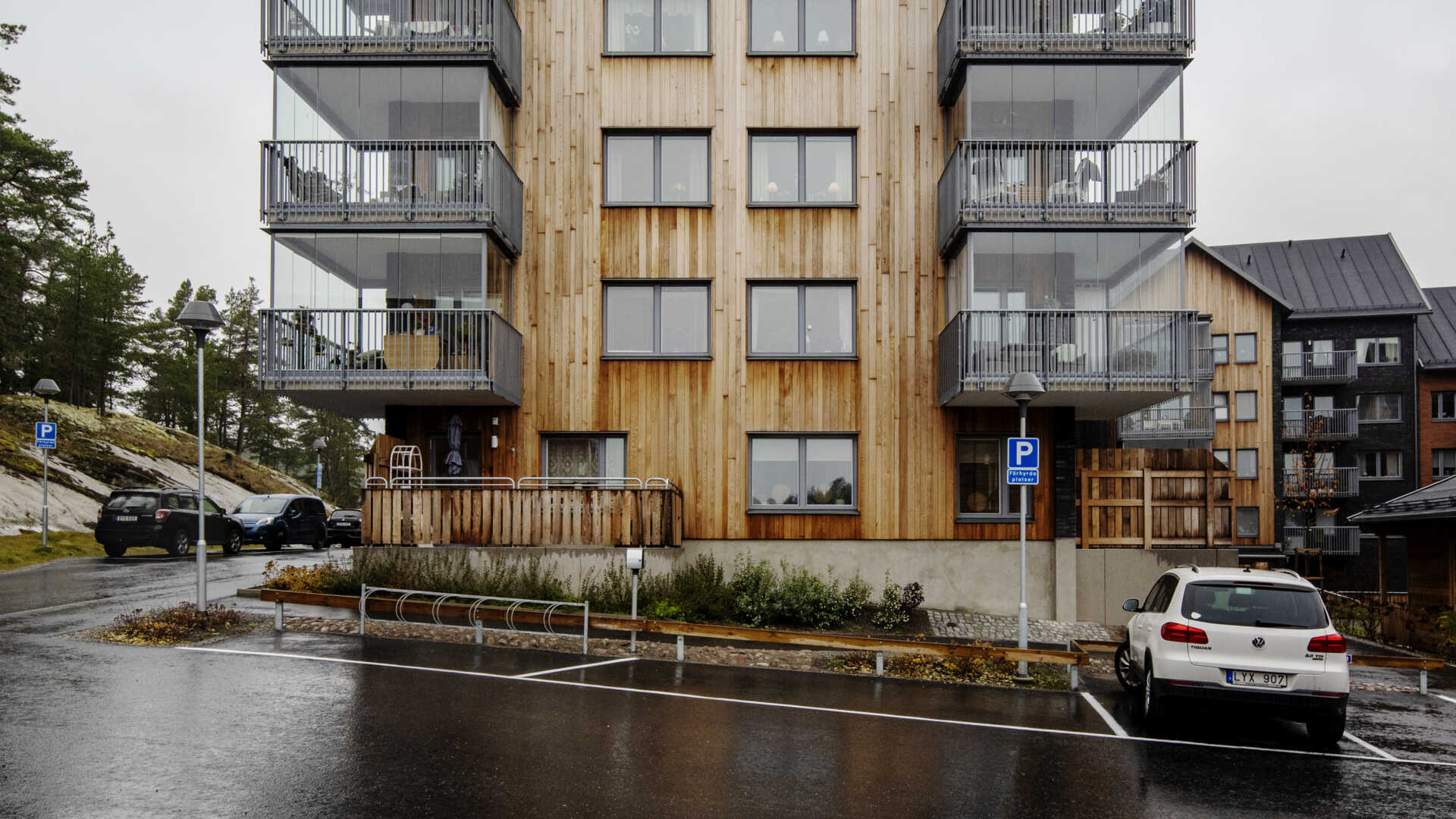 Flerfamiljshus med träfasad och glasade balkonger, parkering och omgivande träd