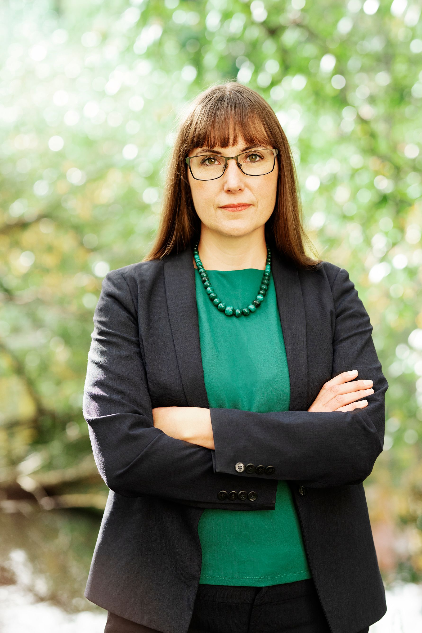 Porträtt av en kvinna med korsade armar, i svart kavaj och grön topp, mot grön bakgrund