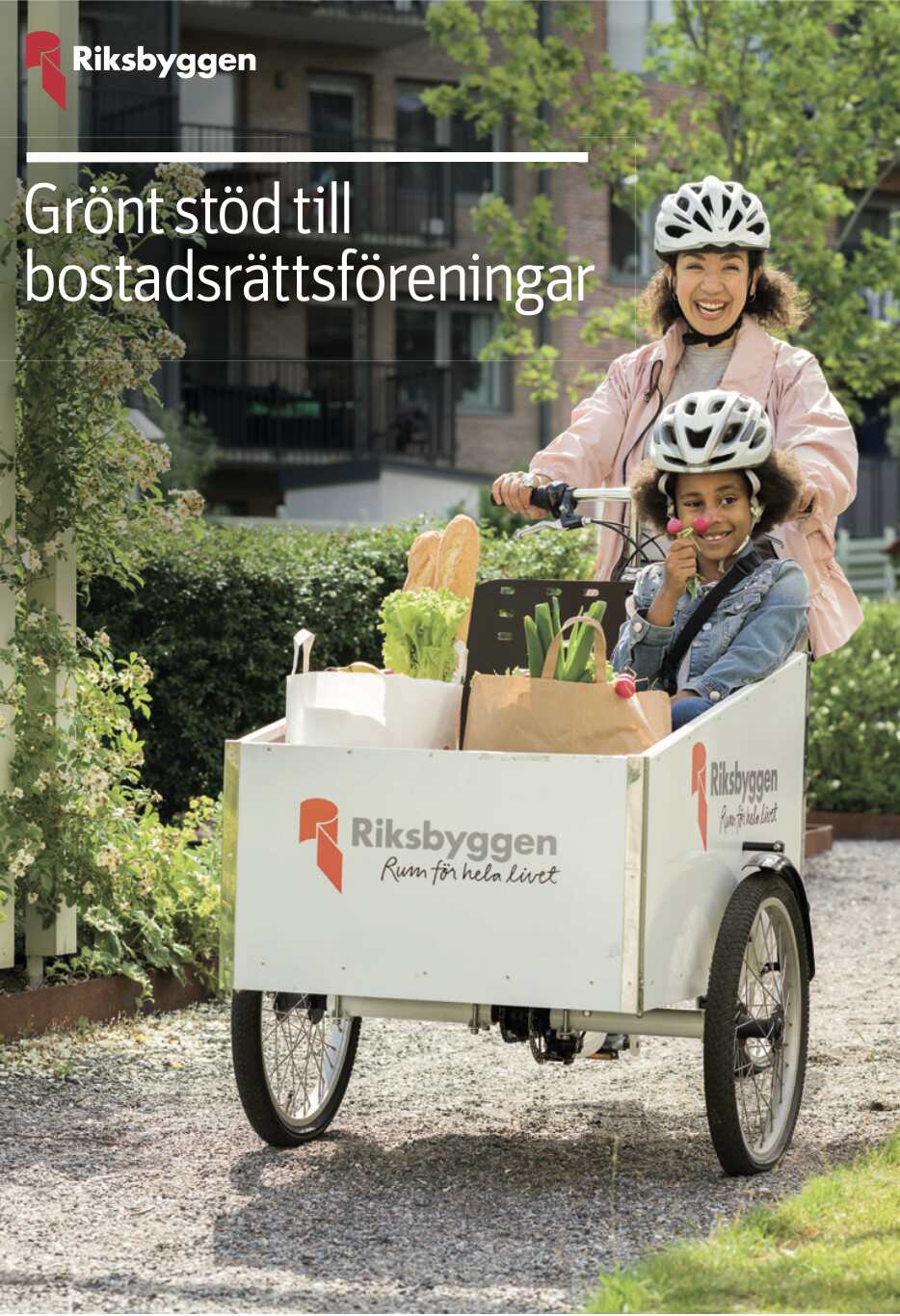 Kvinna och barn i cykelvagn med hjälmar, lastad med grönsaker och hushållsprodukter, framför ett bostadsområde. Texten 