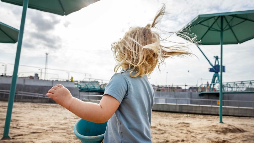 Barn med blont hår som leker på en sandstrand med vind i håret