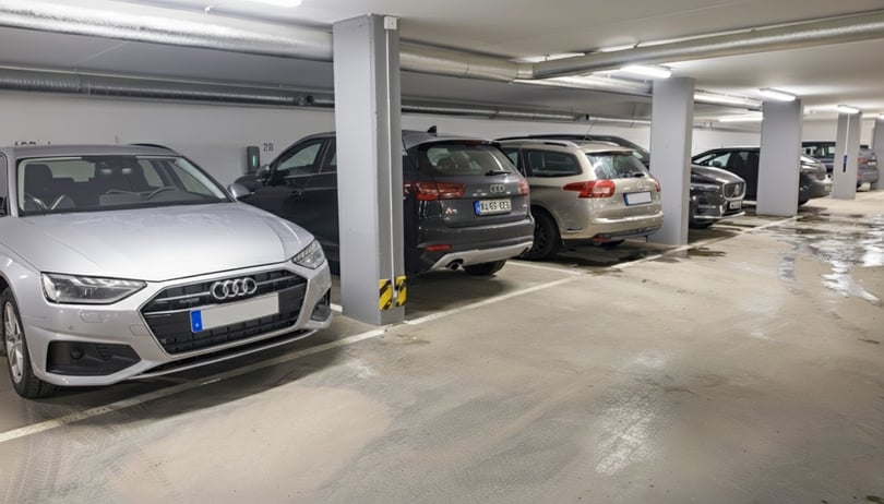 Bilar parkerade i en underjordisk parkeringsgarage med gråa betongväggar och vått golv